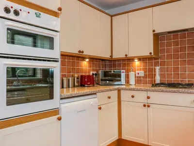 a kitchen with white cabinets and white appliances at Sarah's Cottage in Padstow