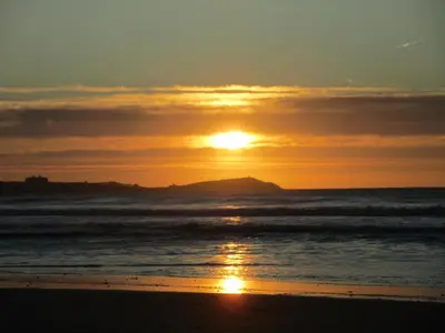 a sunset on the beach with a mountain in the background at Cornish Holiday - Meadow Rise in Saint Columb Major