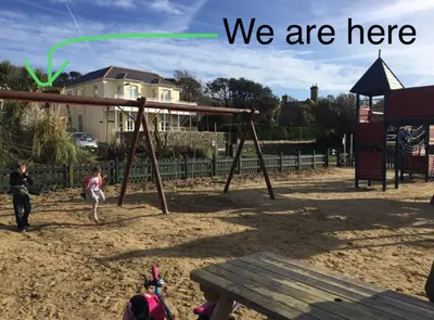 two children playing on a swing set in a park at Sandpiper, apartment across from the beach in Marazion