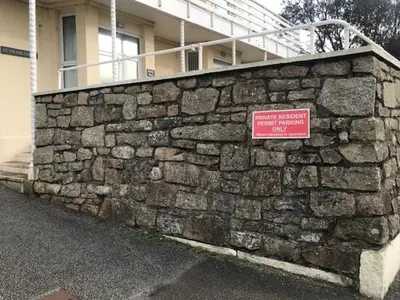 a stone wall with a sign in front of a building at Sandpiper, apartment across from the beach in Marazion