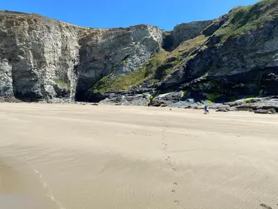 a person walking on a beach next to a cliff at Buena Vista in Tintagel