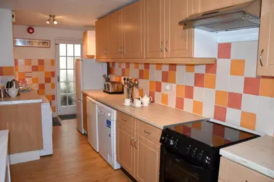 a kitchen with wooden cabinets and a black stove top oven at Newquay Escape, 5 spacious ensuite bedrooms & parking- Simplycheckin in Newquay