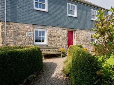 a stone house with a red door and a bench at Rosecott in St Ives