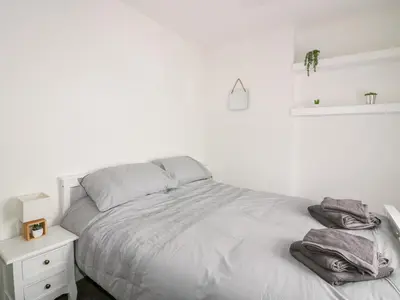a white bedroom with a bed and a night stand at Fistral Quay in Newquay