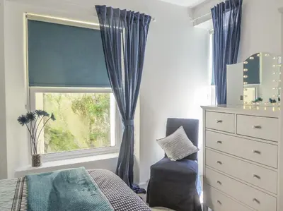 a bedroom with a window with blue curtains and a dresser at Harbour View Apartment in Looe