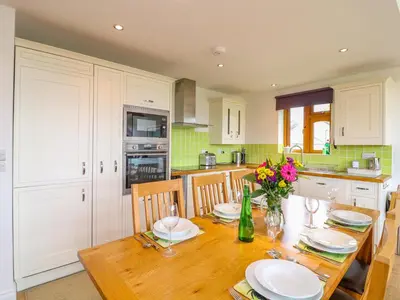 a kitchen with a wooden table with plates and flowers at Kingcup Cottage in Saint Columb Major