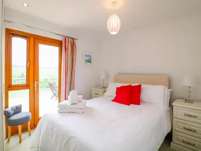 a bedroom with a large white bed with red pillows at Kingcup Cottage in Saint Columb Major