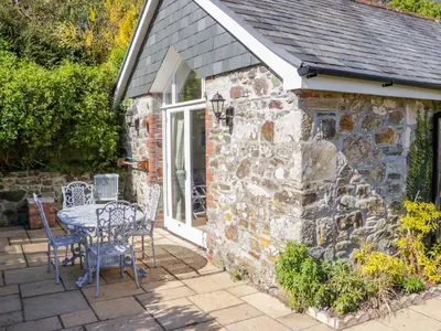 a stone cottage with a table and chairs on a patio at FernGully in Saint Columb Major