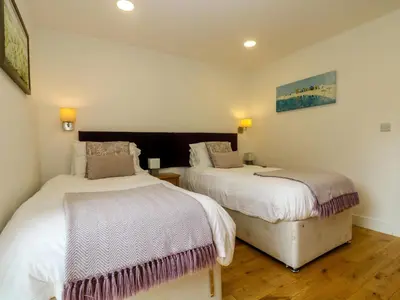 two beds in a room with white walls and wooden floors at Maple in Truro