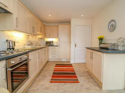 a kitchen with wooden cabinets and a rug on the floor at Cornflower Cottage in Saint Columb Major
