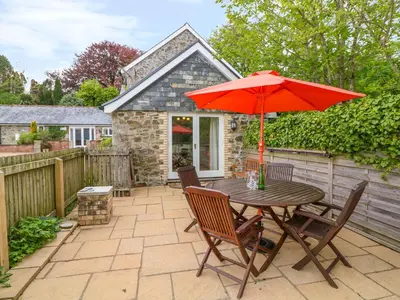 a wooden table with a red umbrella on a patio at Cornflower Cottage in Saint Columb Major
