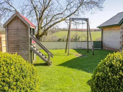 a playground in a yard with a wooden swing at Lambkin Cottage in Saint Columb Major