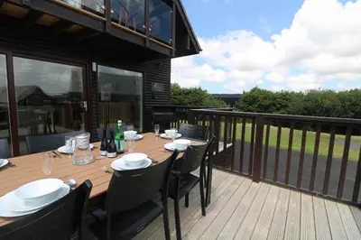 a wooden deck with a table and chairs on a balcony at Willow, Retallack in Saint Columb Major