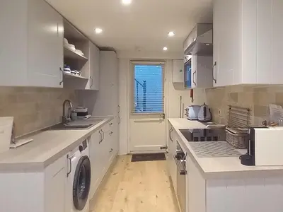 a kitchen with white cabinets and a washer and dryer at Below Deck in Fowey