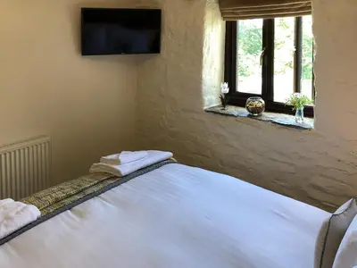 a bedroom with a bed with white sheets and a television at Cider Press Cottage in Fowey