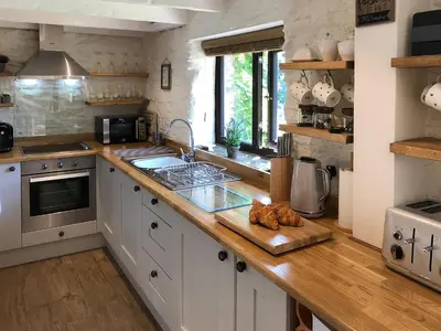 a kitchen with white cabinets and a wooden counter top at Cider Press Cottage in Fowey