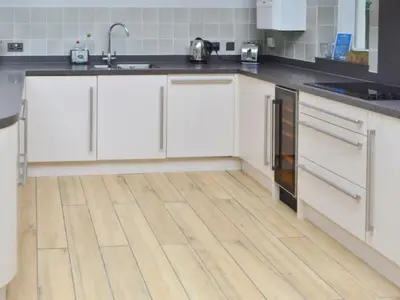 a kitchen with white cabinets and a wooden floor at St Monicas in Fowey