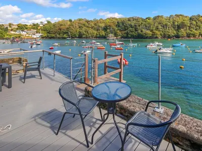 a deck with chairs and a table and boats in the water at Tarquins in Fowey