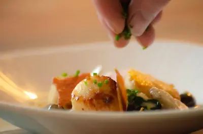 a person sprinkling green onions on a plate of food at Molesworth Arms in Wadebridge