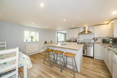 a kitchen with white cabinets and a island with bar stools at Penbarden Barn in Bude