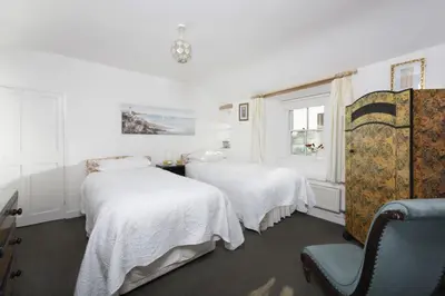 a white room with two beds and a chair at Trevara, Marazion in Marazion