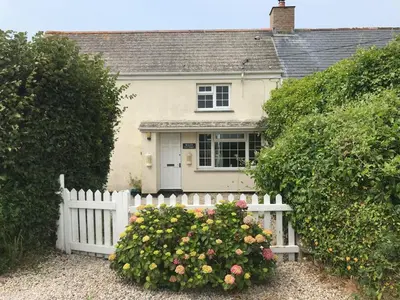 a white fence in front of a house with flowers at Bejowan Cornish Cottage in Newquay