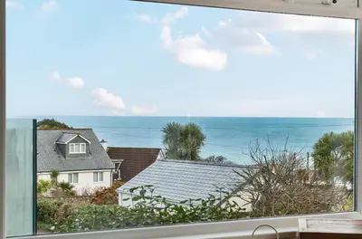 a window with a view of a house and the ocean at Lamorna Lodge in St Ives