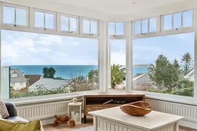 a living room with large windows and a table at Lamorna Lodge in St Ives