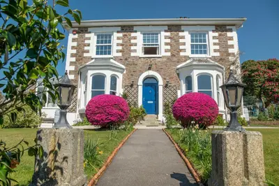 a brick house with a blue door and pink flowers at Ivy House Cornwall B&B in St Austell