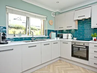 a kitchen with white cabinets and blue tiles at Apartment 8 in Newquay