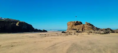 a beach with a rock with a flag on it at Ocean's Eddge, Perranporth in Perranporth