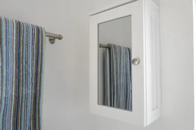 a mirror in a white cabinet with striped towels at Krissie's in Marazion