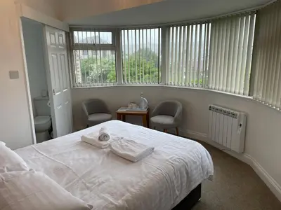 a bedroom with a bed and two chairs and windows at The Mandalay Guest House in Mevagissey