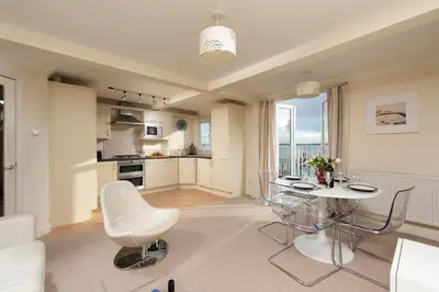 a living room with a table and a kitchen at Waves Apartment, St Ives in St Ives