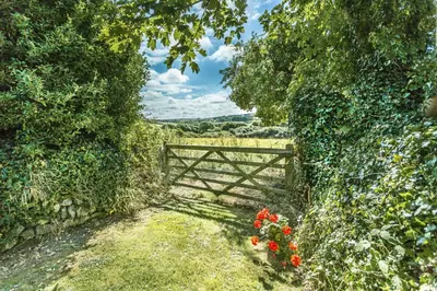 an open gate in a field with red flowers at Pear Tree Barn - Amazing Country views - Pet friendly - Balcony in Newquay