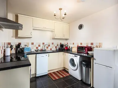 a kitchen with white cabinets and a washer and dryer at Nectan in St Austell