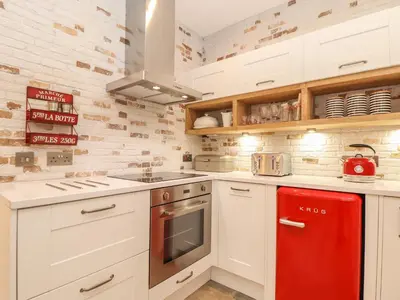 a kitchen with white cabinets and a red refrigerator at Beach Hut in Tintagel