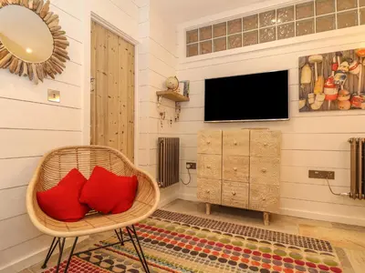 a living room with a wicker chair with red pillows at Beach Hut in Tintagel