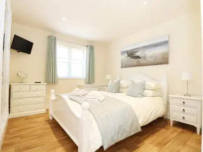 a white bedroom with a white bed and a television at Elm Cottage in Truro