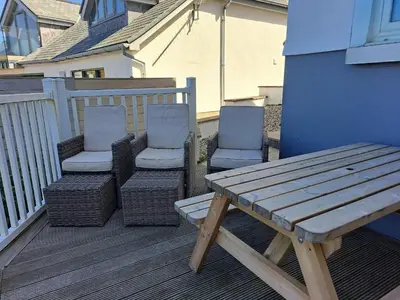 a wooden bench and two chairs on a deck at Seagulls Perch in Mawgan Porth