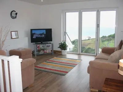 a living room with a couch and a tv and windows at Seagulls Perch in Mawgan Porth