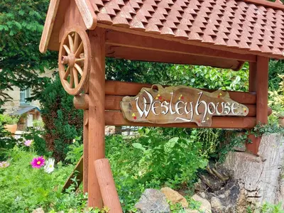 a wooden sign in a garden with a sign at Wesley House Holidays - Choice of 2 Quirky Cottages in 4 private acres in Redruth