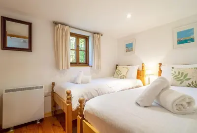 a bedroom with two beds and a window at Church Close Cottage in Gwennap