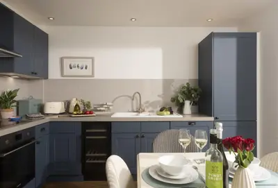 a kitchen with blue cabinets and a table with wine glasses at Cob Cottage in St. Agnes