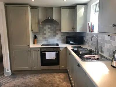a kitchen with white cabinets and a sink and a stove at Bay House Lobber Port Isaac Apartment with Sea Views & Parking in Port Isaac