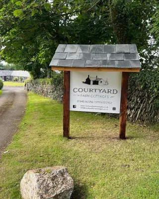 a sign in the grass next to a road at Courtyard Farm Cottages in Boscastle