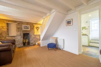 a living room with a staircase and a blue chair at Balwest Cottage in Helston