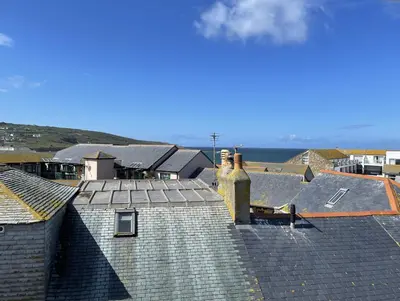 a view of roofs of houses with the ocean in the background at Porthia Cottage in St Ives
