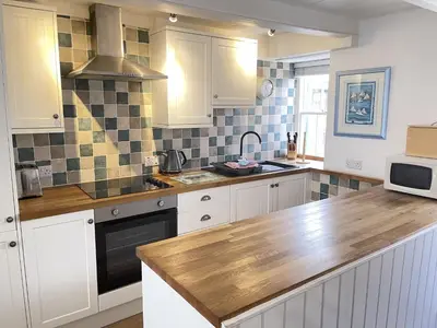 a kitchen with white cabinets and a wooden counter top at Porthia Cottage in St Ives
