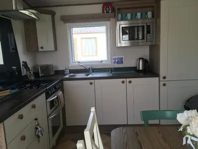 a kitchen with white cabinets and a sink and a window at BRANWOOD Luxury Caravan Holidays Newquay in Newquay